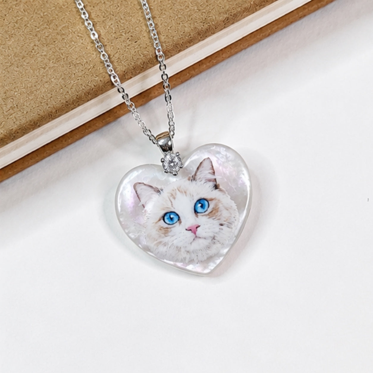 Hand-painted pet portrait pendant displayed on a silver chain with a blue-eyed white cat portrait.