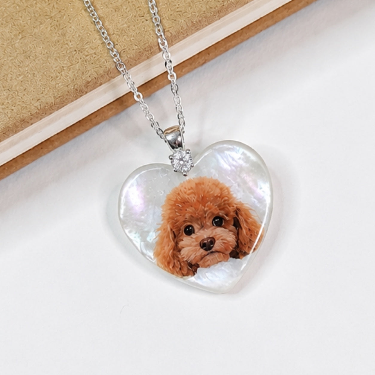 Hand-painted pet portrait pendant displayed on a silver chain with a curly brown dog portrait.