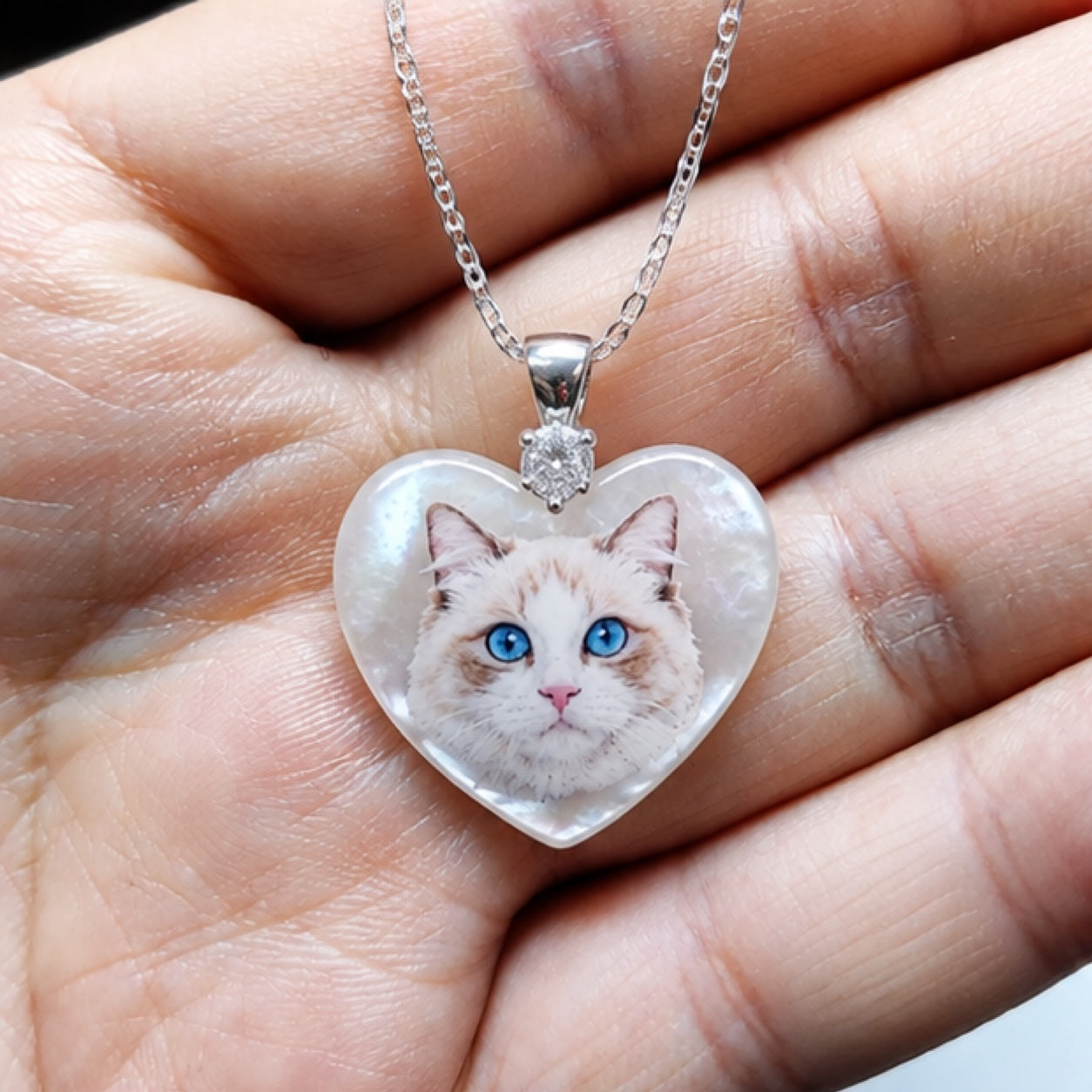 Hand-painted pet portrait pendant with a blue-eyed white cat painted on a heart-shaped mother-of-pearl piece.
