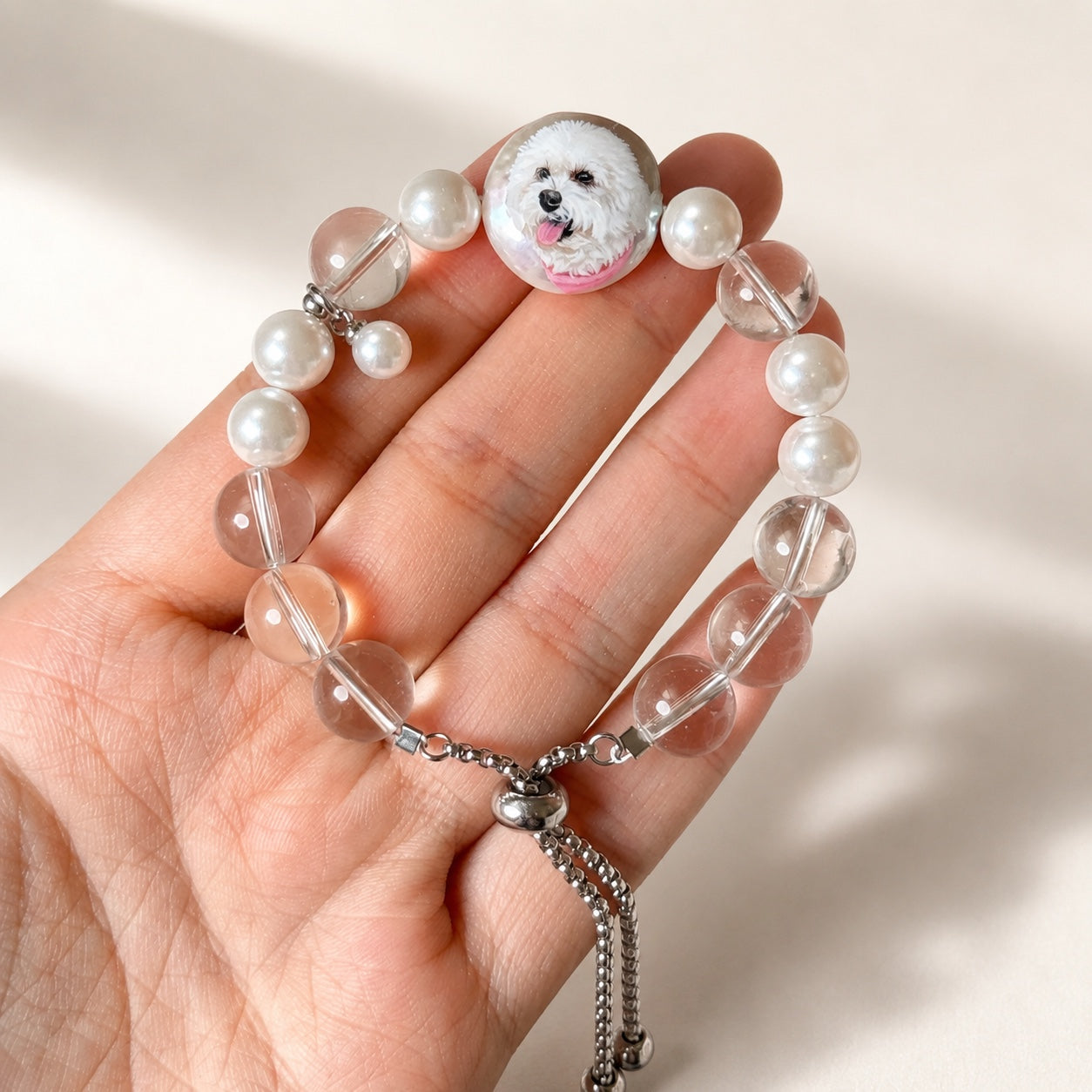 Custom pet face bracelet held in a hand to show the two pet portrait charms and crystal beads.