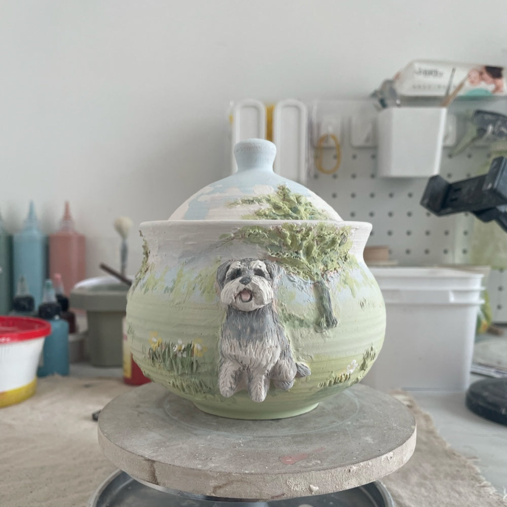 Custom ceramic pet urn in a beach scene displayed with the reference photo of the black and white dog used for the sculpture.