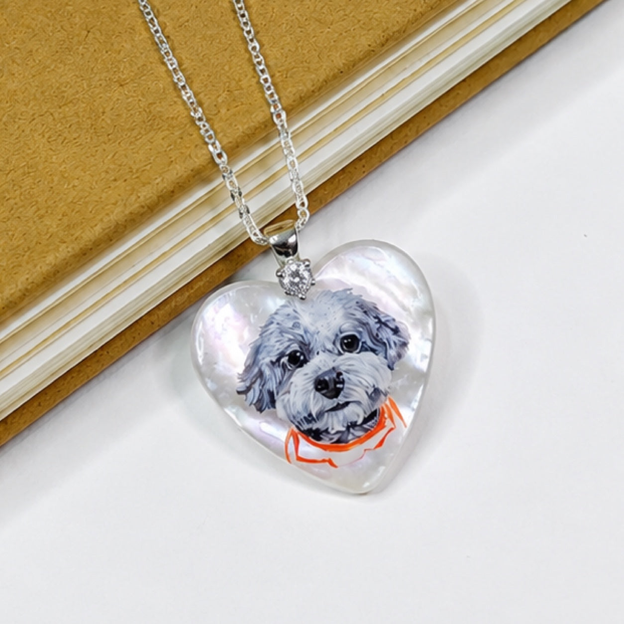 Hand-painted pet portrait pendant displayed on a silver chain with a gray dog portrait and red collar.
